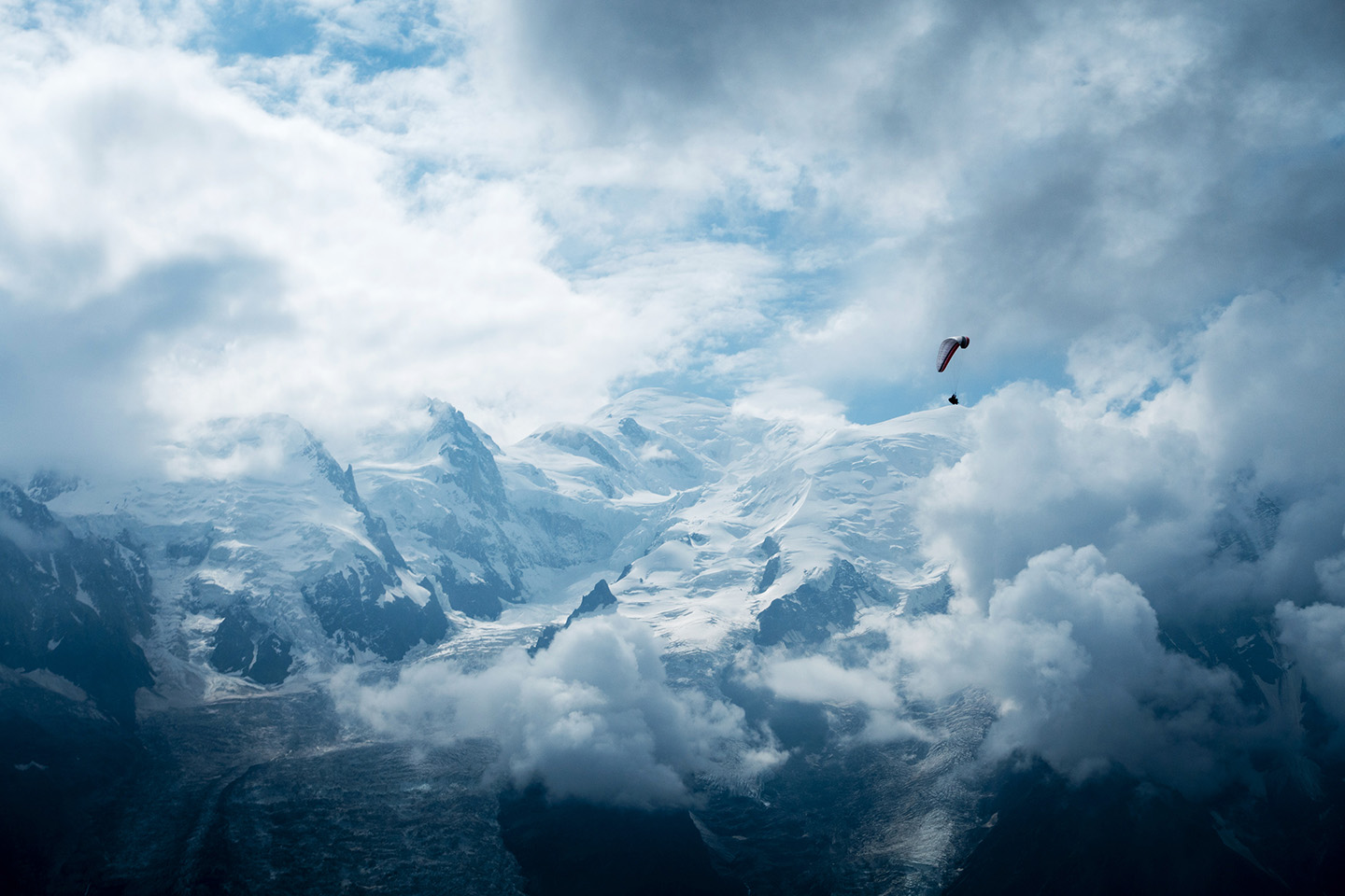 A paraglider in the mountains above a valley of cloud